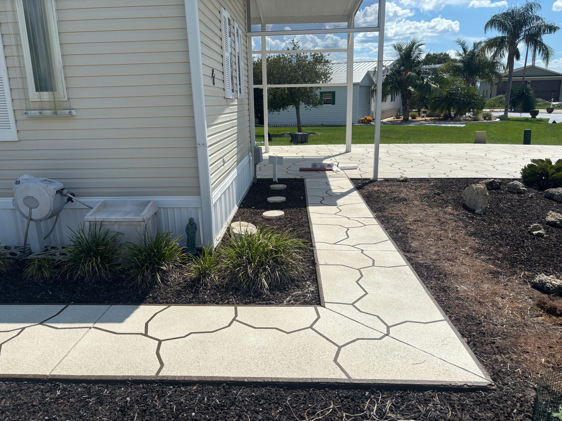 A paved walkway leads to a beige house with a porch. Brown mulch borders the path.