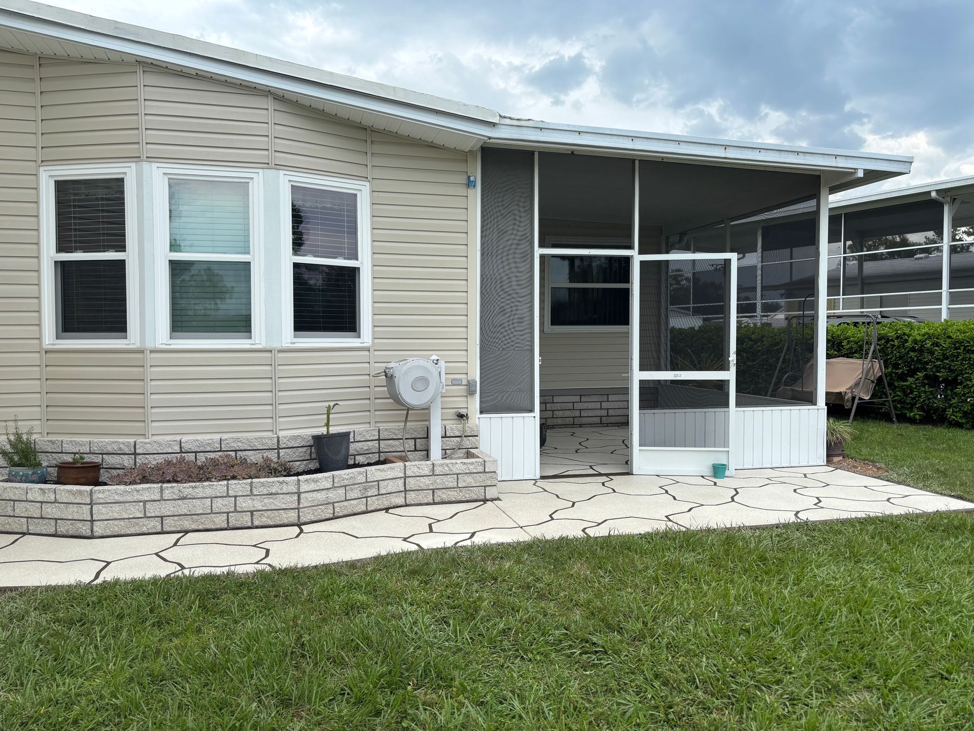 A beige house with a screened porch, small garden, and green lawn on an overcast day.