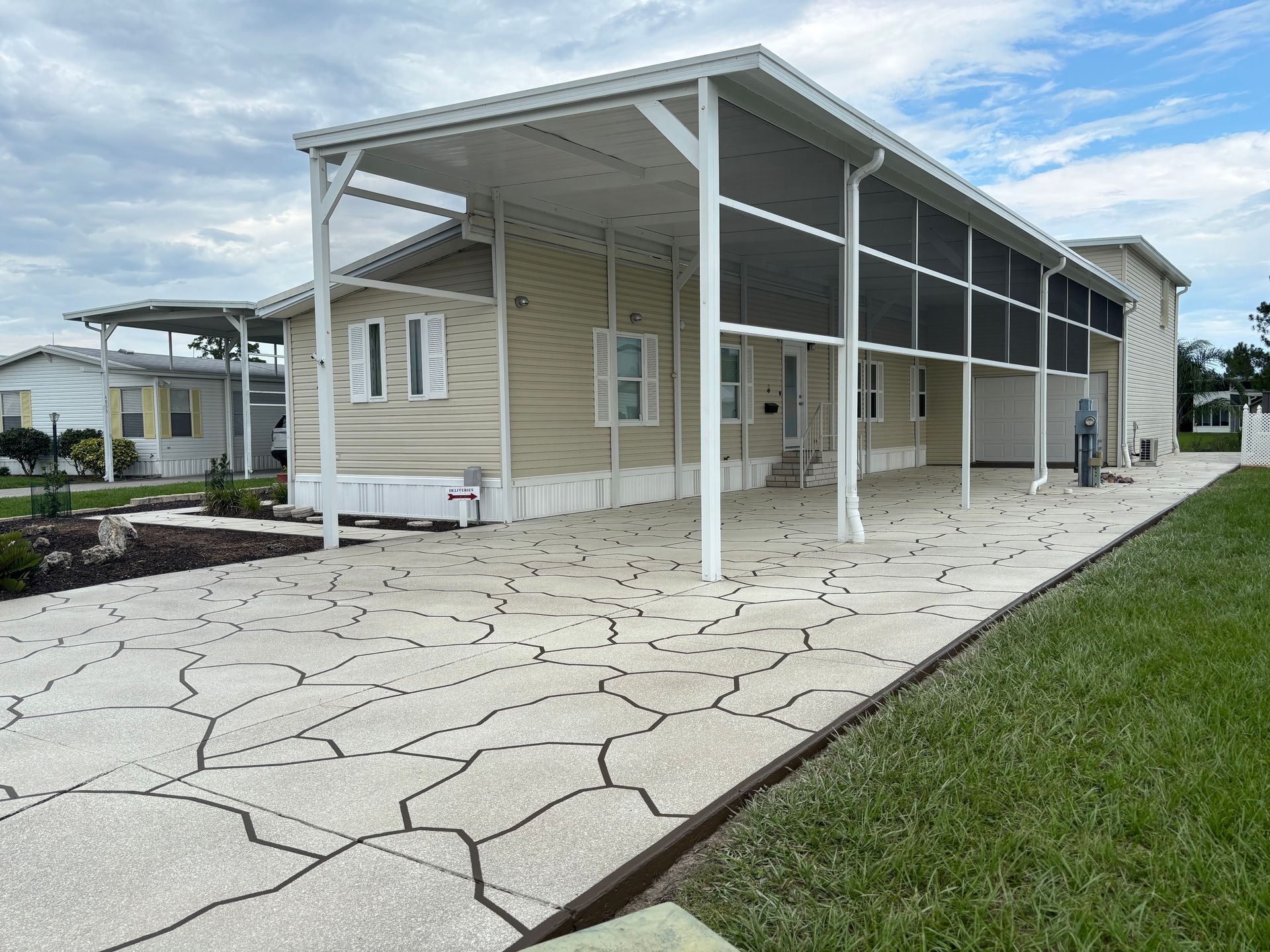 Tan house with covered screen porch and patterned driveway.