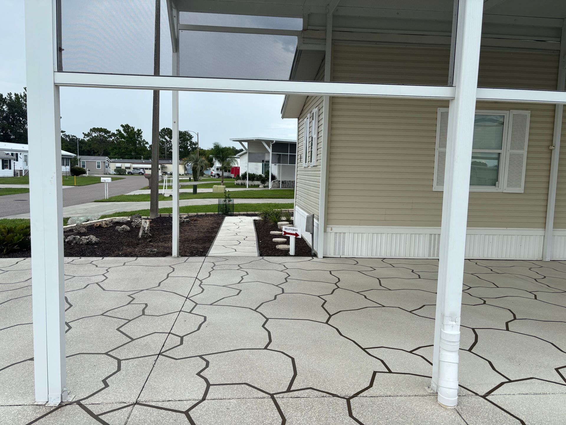 View from porch looking at a house in a mobile home park. Paved patio, beige siding, white trim.