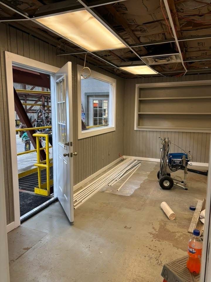 Interior of room under construction with a door open to an outdoor ramp, a window, and painting equipment.