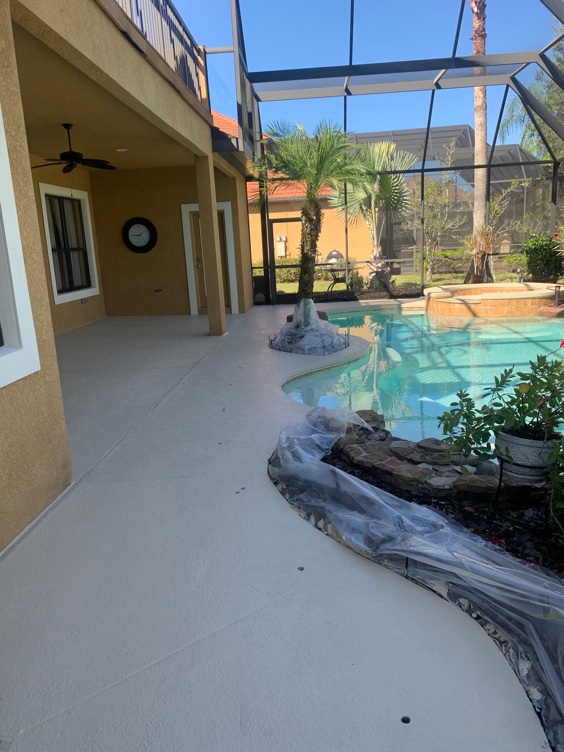 Poolside patio with a pool, a covered area, and a yellow stucco wall.