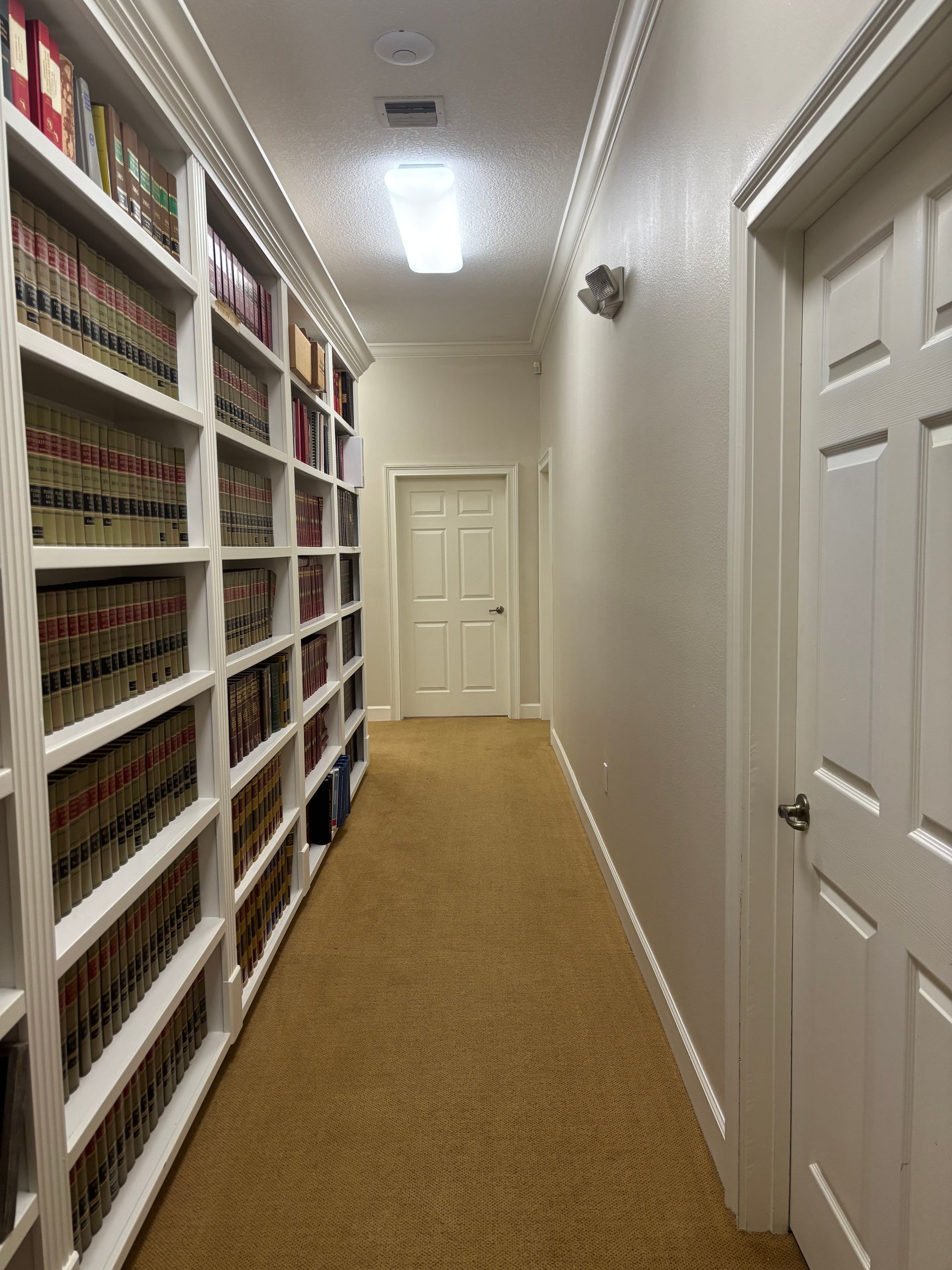 Hallway with bookshelves on the left, a closed door at the end and on the right. Beige carpet.