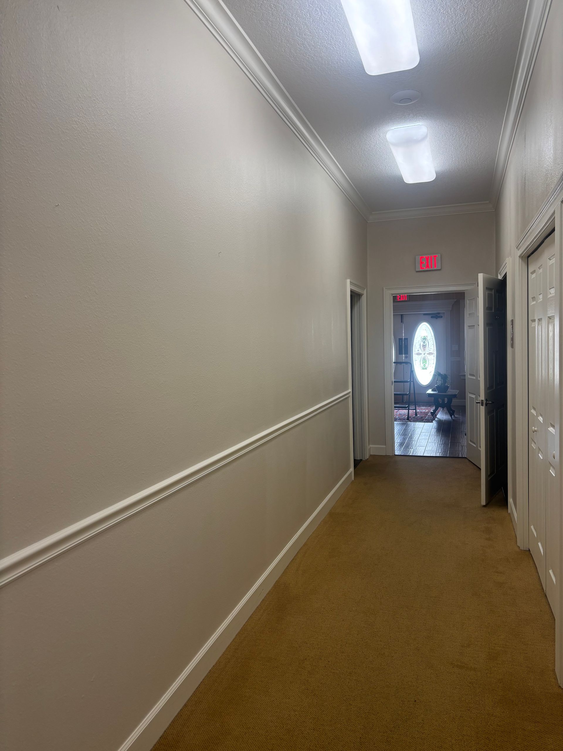 Narrow beige hallway with crown molding, carpet, and a view to a door and exit sign.