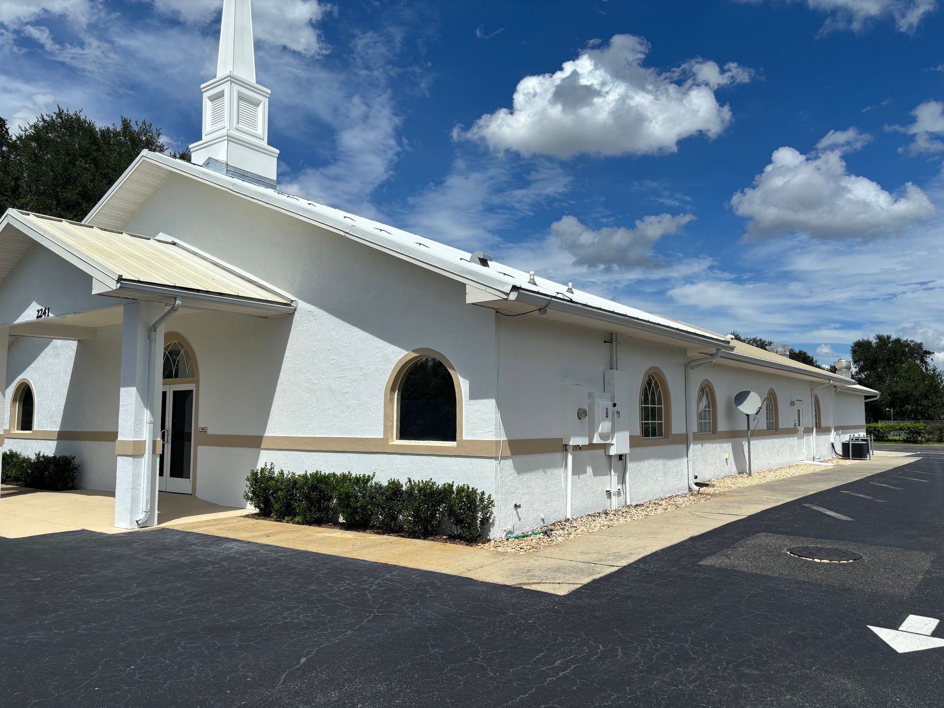 White church building with steeple and arched windows against a blue sky with clouds.