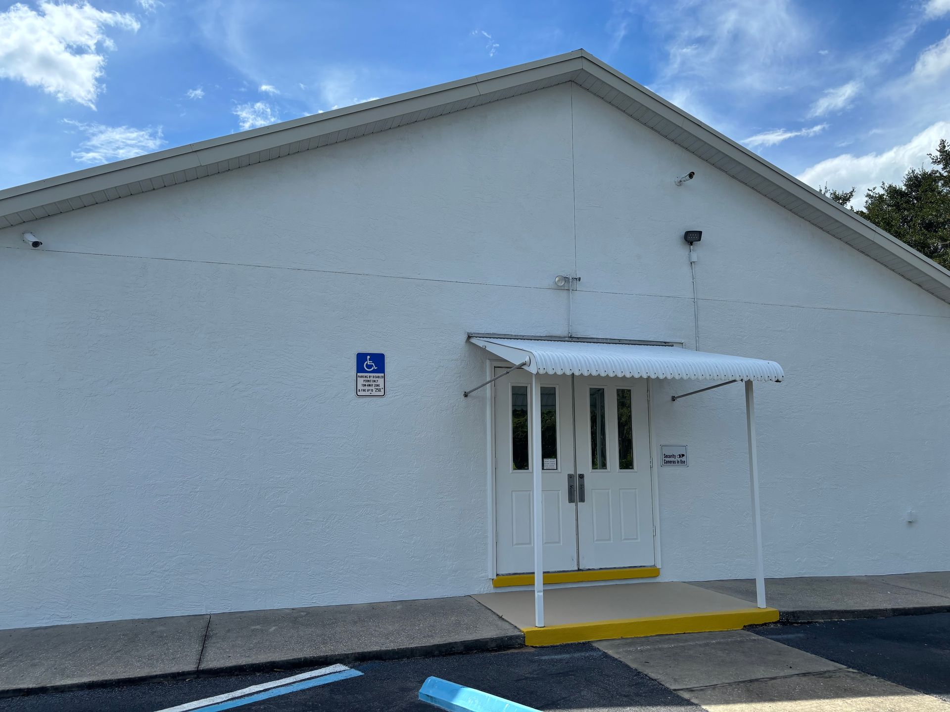 White building entrance with awning, accessible parking sign, and double doors.