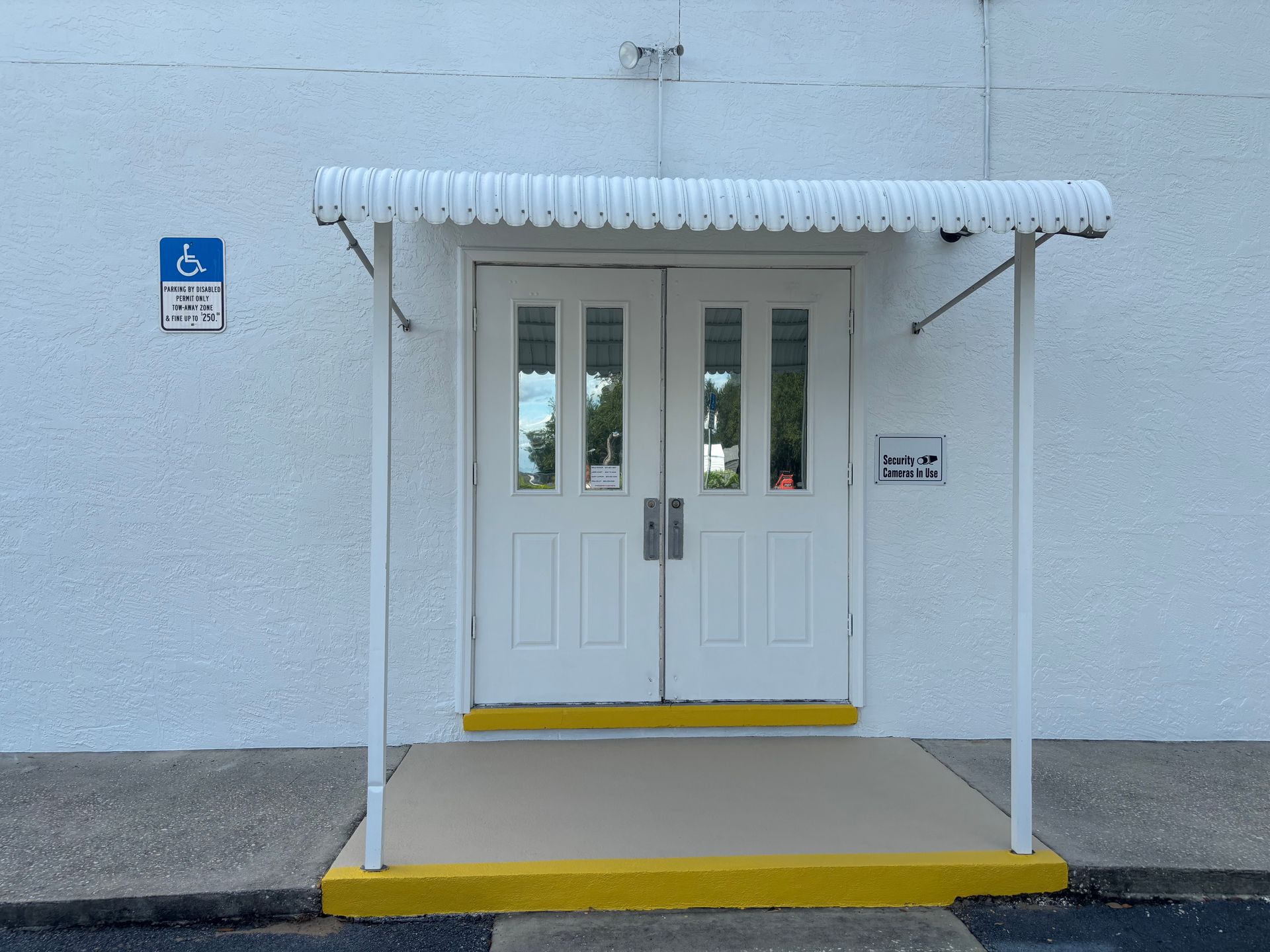 White double doors under a white awning, wheelchair-accessible sign, building with white walls, yellow trim.