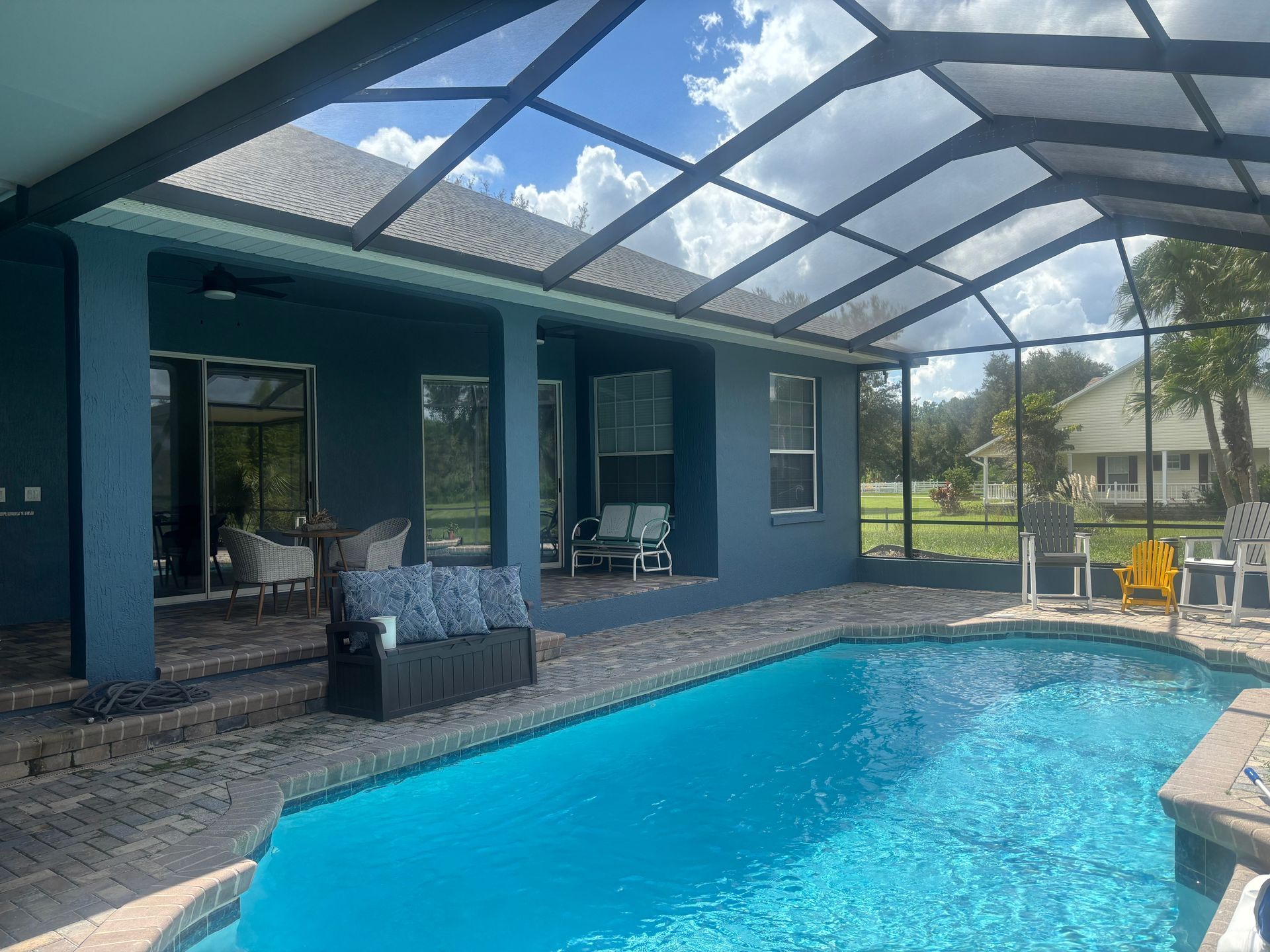 Pool with blue water, a screened-in patio, and a teal-colored house on a sunny day.