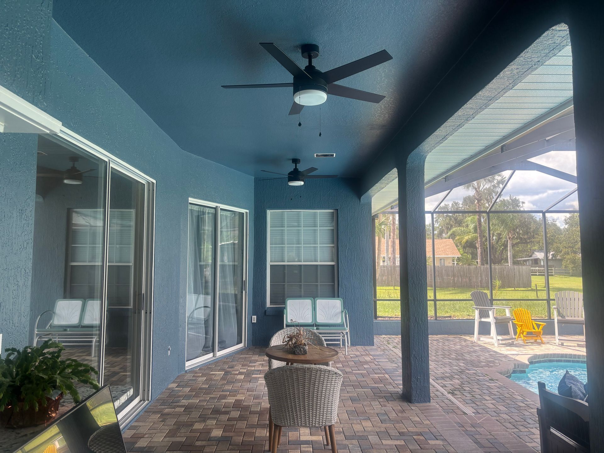 Blue patio with ceiling fans, furniture, sliding glass doors, and a view of a pool.