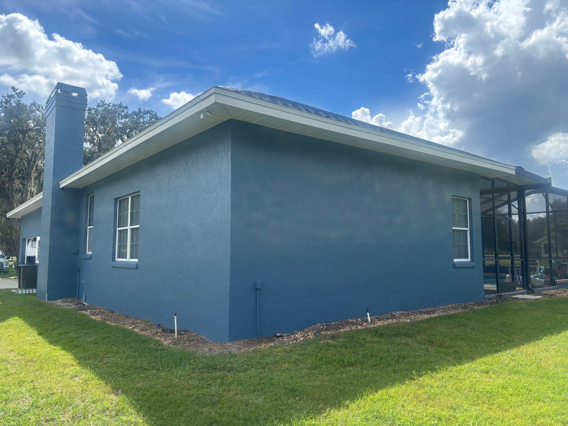 Blue house with white trim, two windows, and a chimney under a bright blue sky with fluffy white clouds.