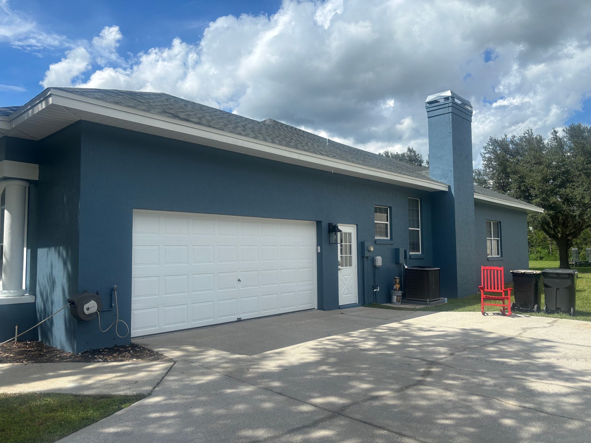 Blue house with white garage door, chimney, and driveway under a cloudy sky.