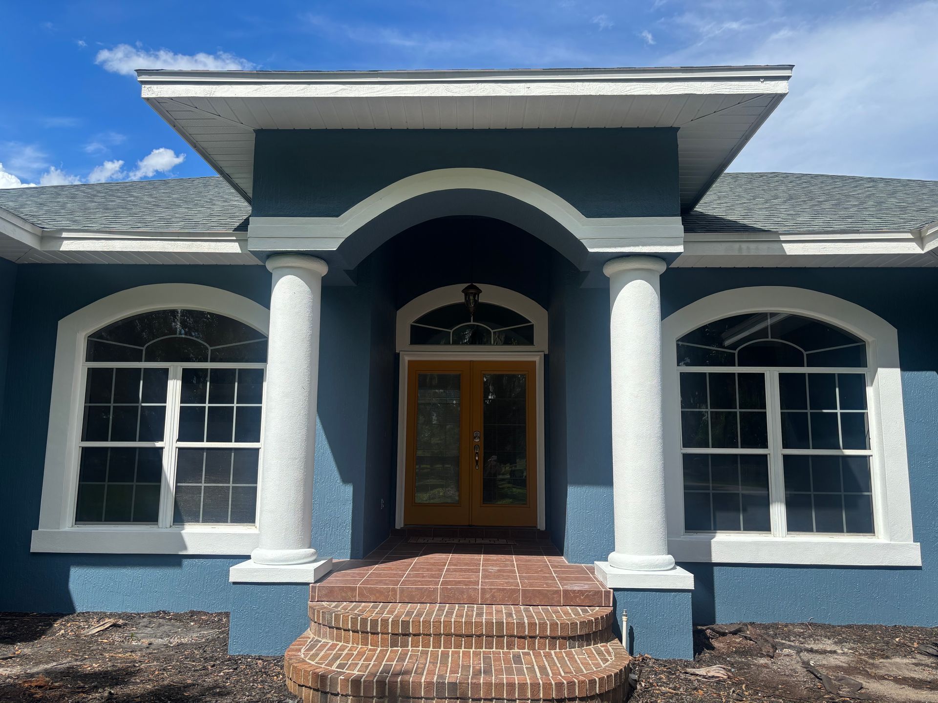 Blue stucco house with white trim, brick steps, and arched entryway.