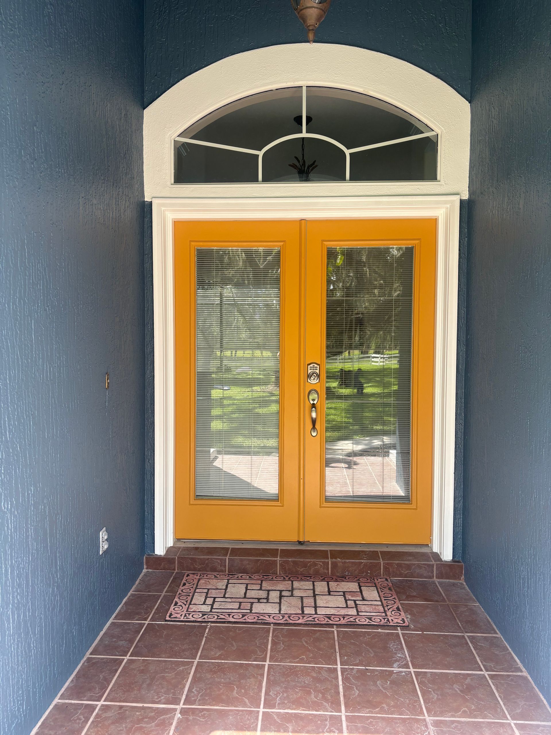 Yellow double doors with glass panels and blinds, beneath an arched window. Blue exterior walls.