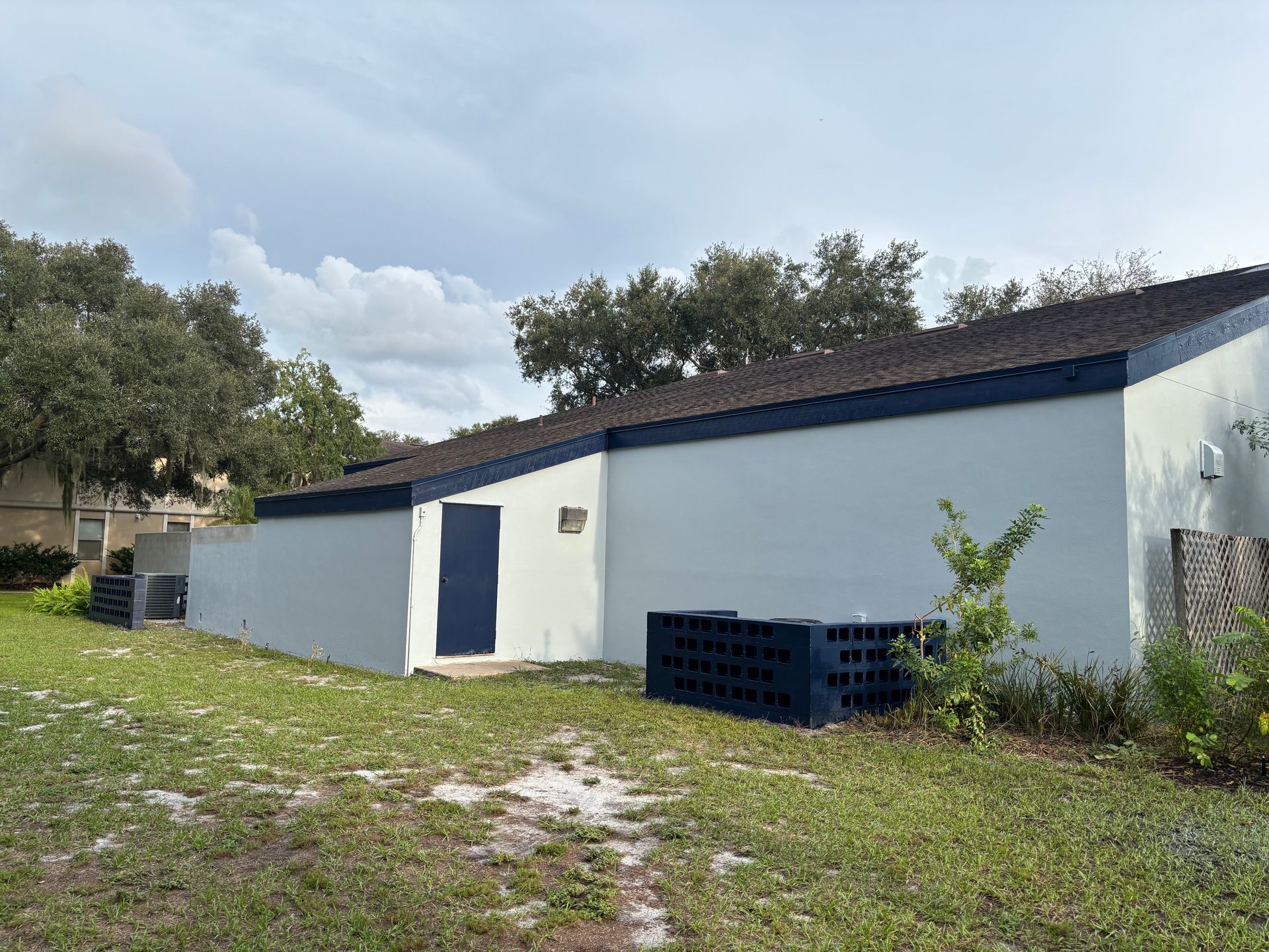 White building with blue trim and door, situated in grassy area with trees.