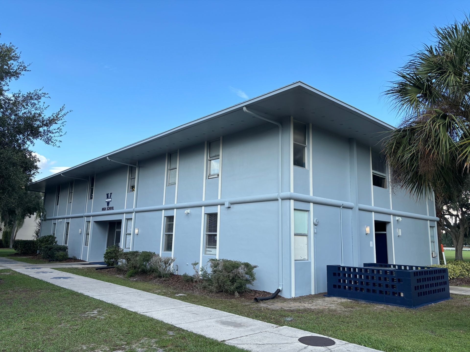 Two-story light blue apartment building under a bright blue sky.
