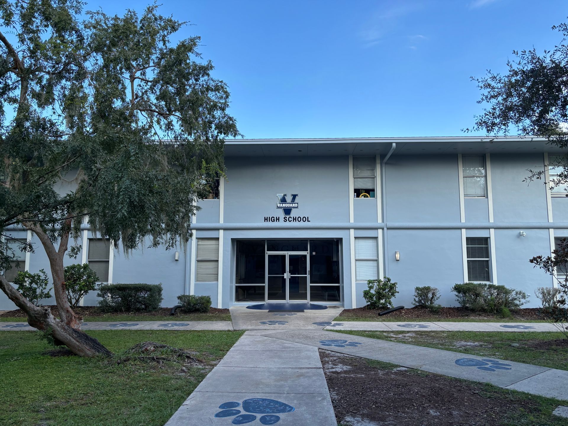 Two-story light blue building with glass entrance. Paw prints on the sidewalk leading to the door, trees surrounding.