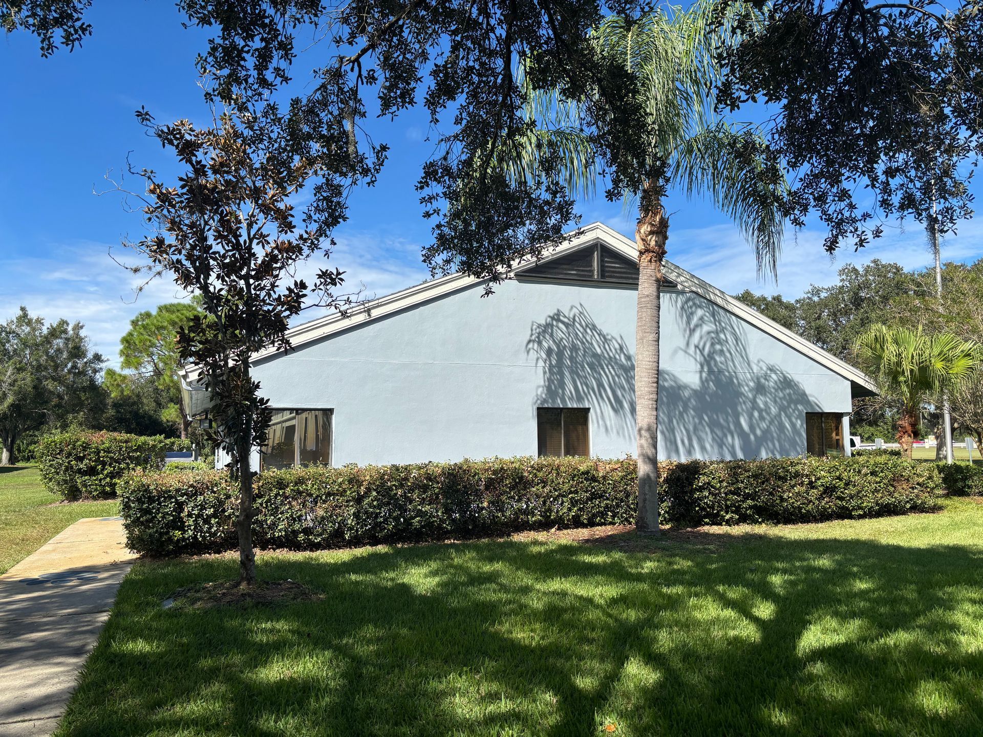 Blue building with hedges and trees under a blue sky.