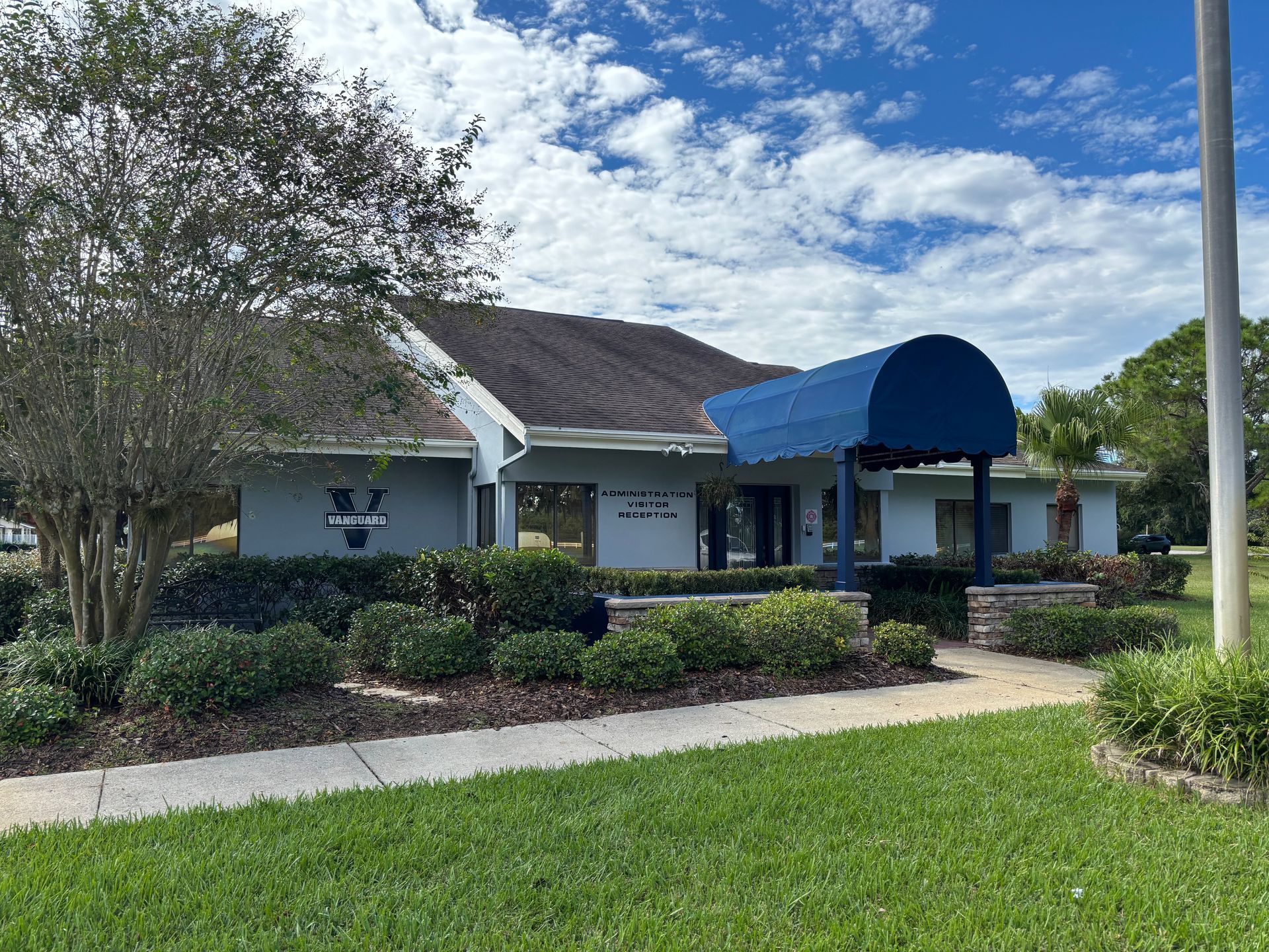 Blue awning over a light blue building, with landscaping and a lawn. Cloudy sky overhead.