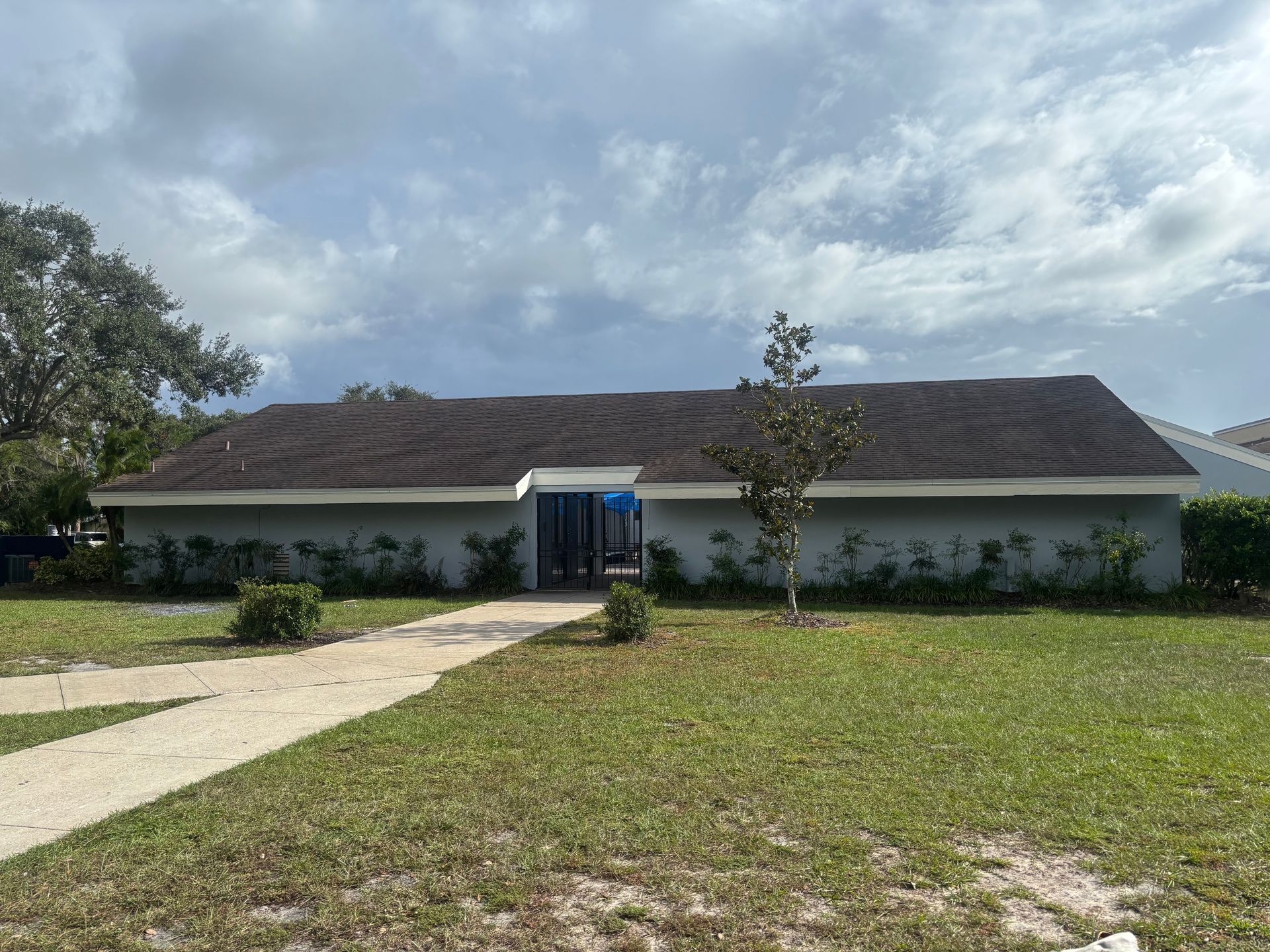 A light blue building with a brown roof, a walkway leading to the front door, and green grass.