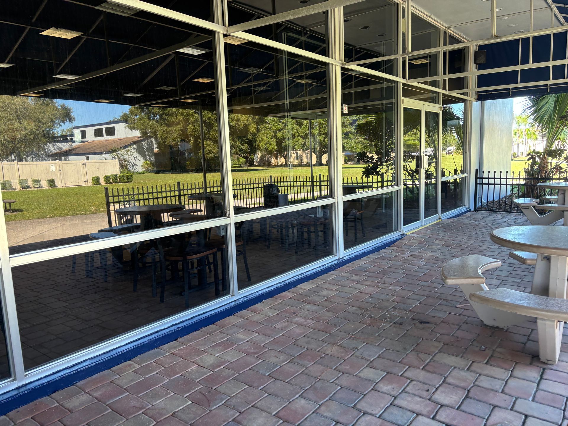 Brick patio with outdoor seating next to a building with large windows overlooking a grassy area with trees.