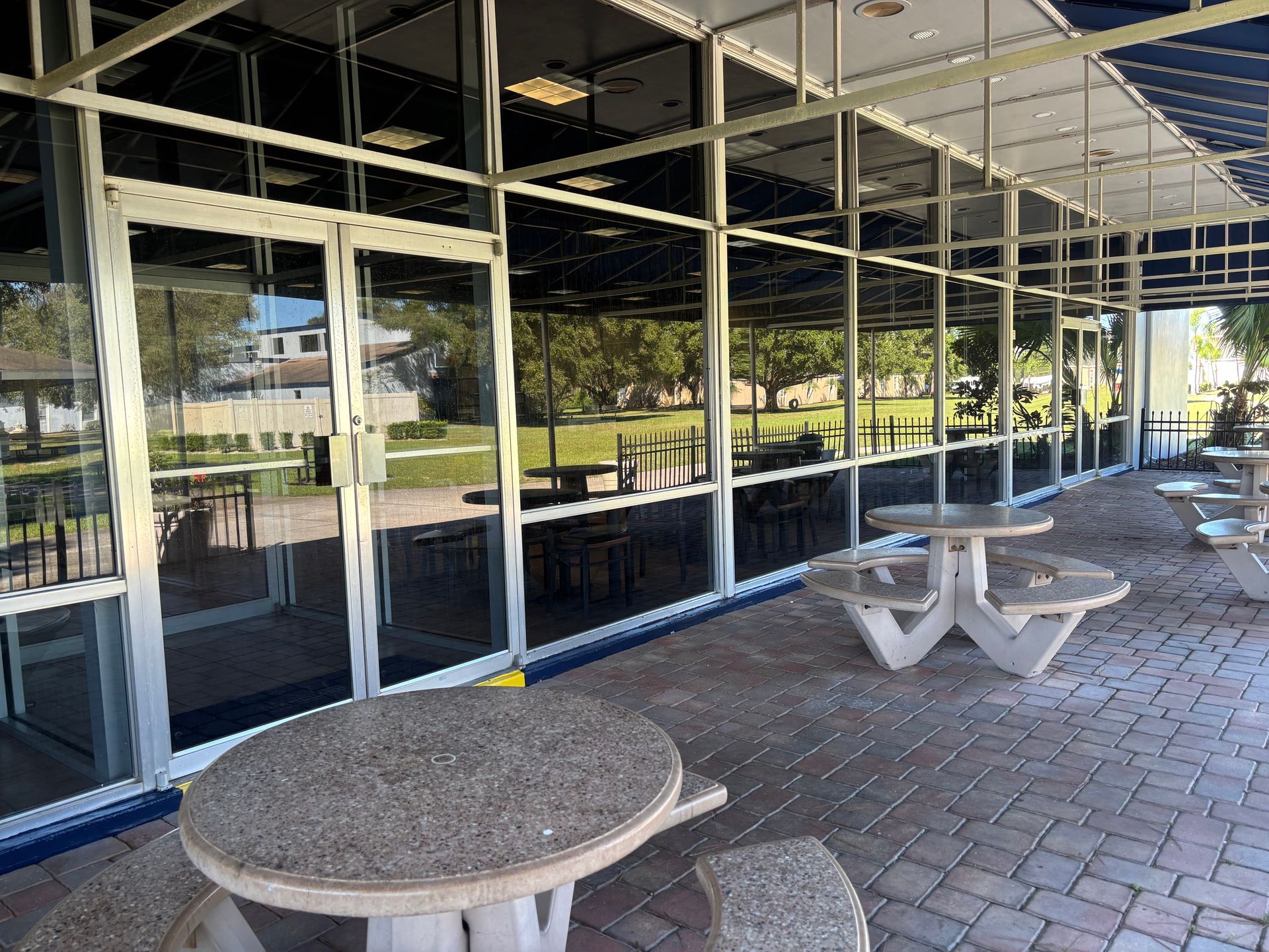 Patio with concrete tables and glass-walled building reflecting a grassy park on a sunny day.