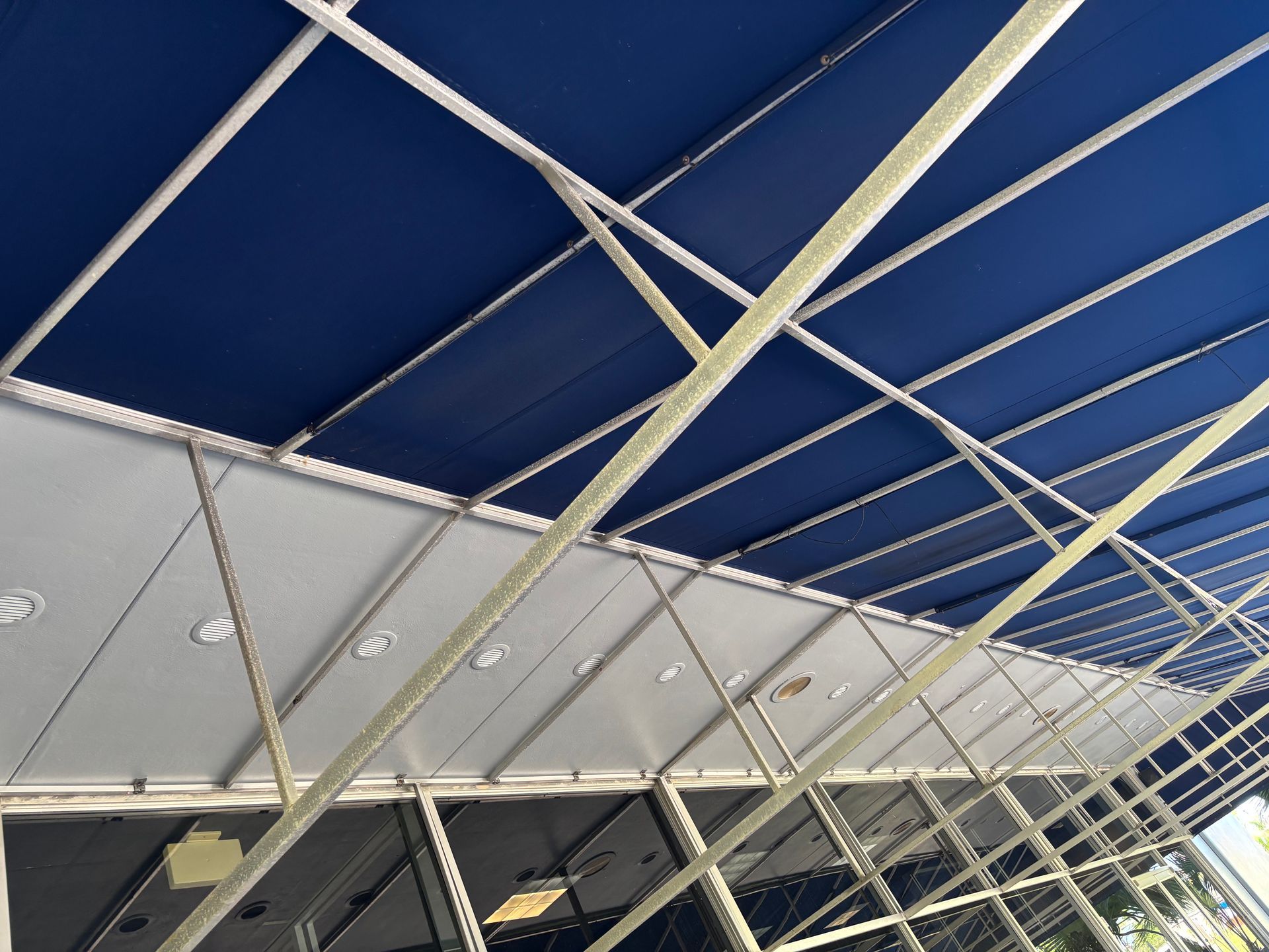 Blue awning over a building with glass windows, supported by a metal framework.