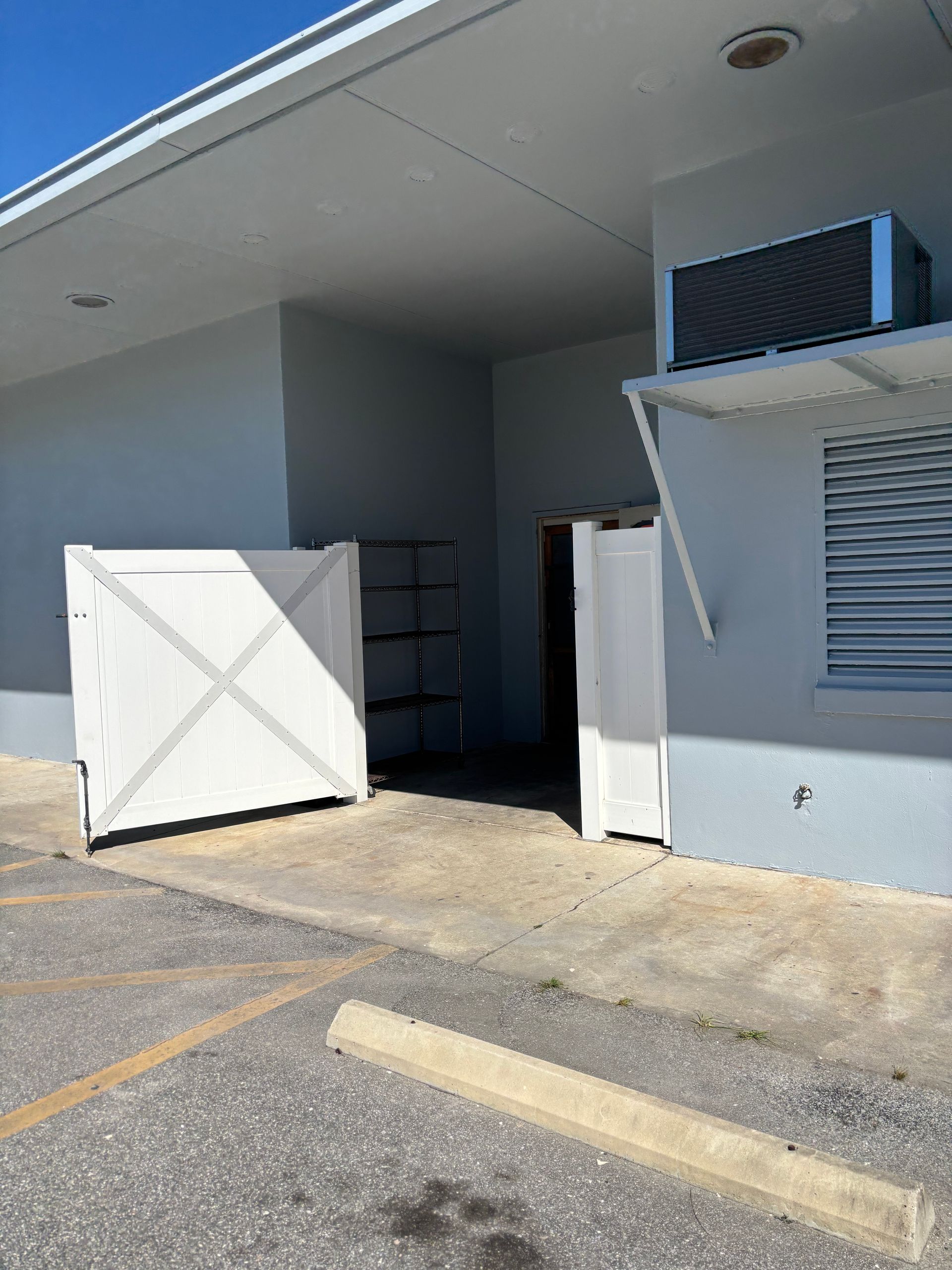 Exterior of a building with a partially open doorway, a white gate, and an air conditioning unit.