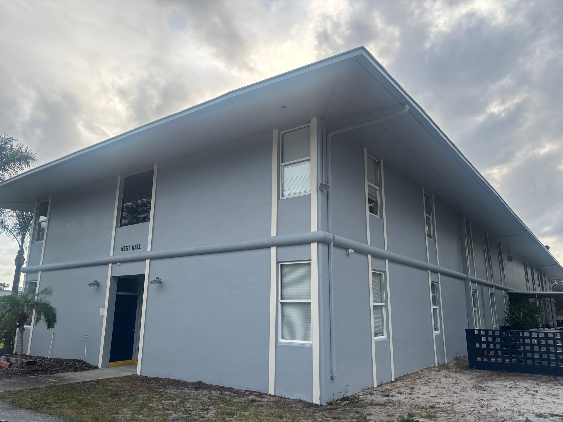 Two-story light blue apartment building with white trim. Overcast sky.
