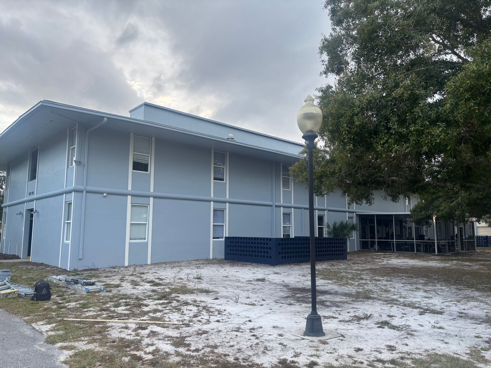 Two-story blue building, white trim, with a streetlight in front and cloudy sky in the background.