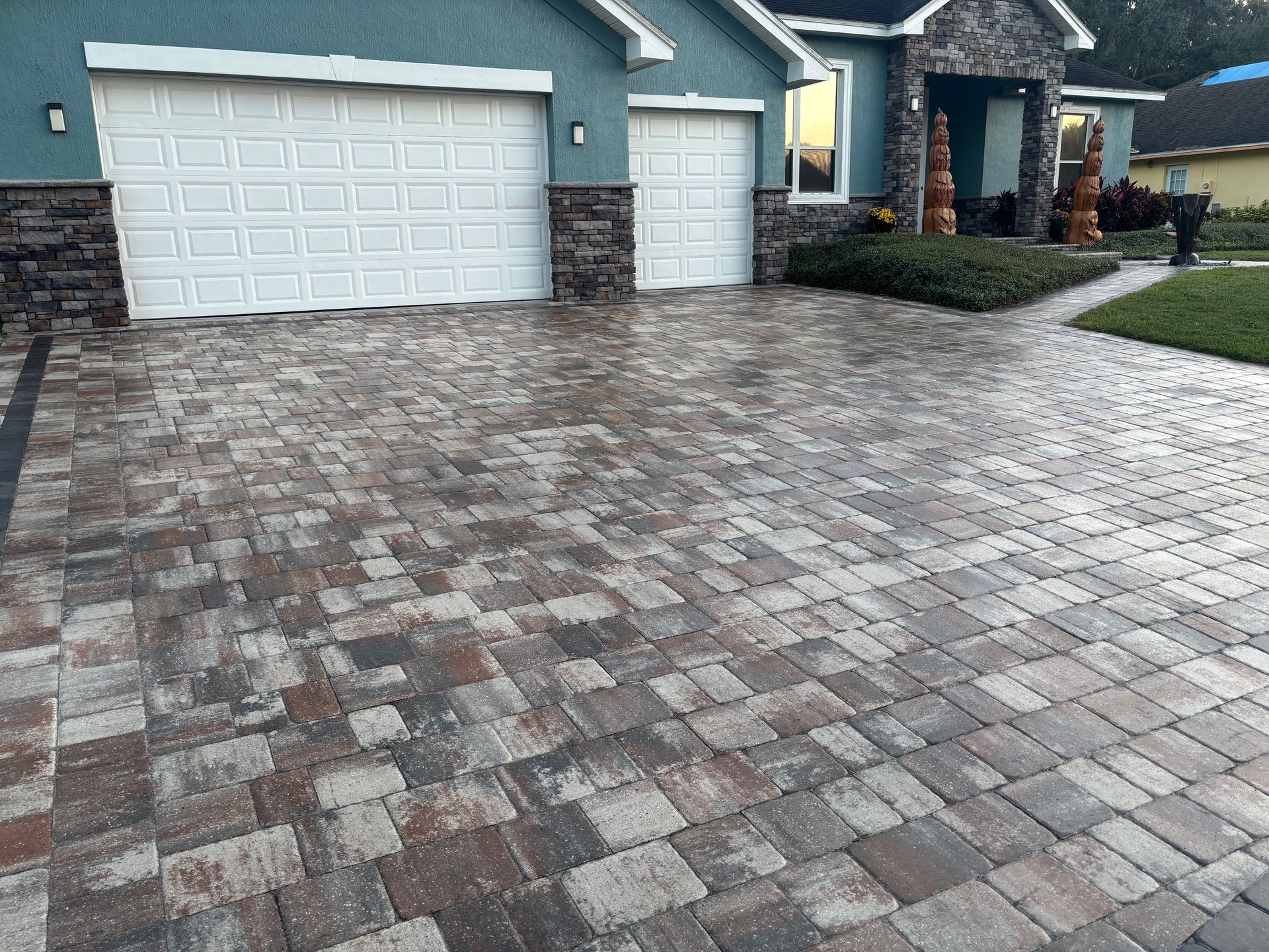 Driveway paved with multi-colored bricks leading to a house with a teal exterior and stone accents.
