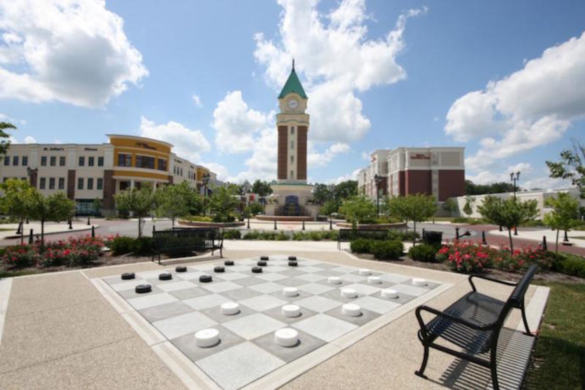 A large checkers board in a park with a clock tower in the background.