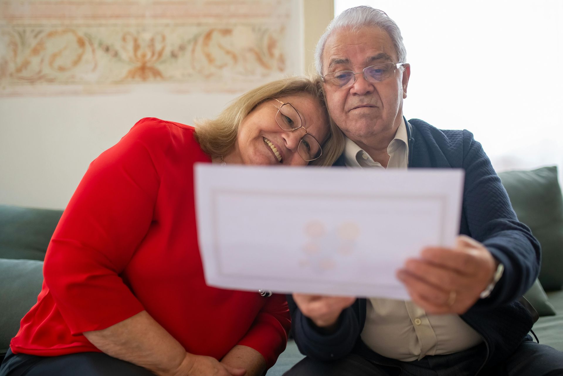 An elderly couple is sitting on a couch looking at a piece of paper.