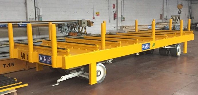 Rimorchio industriale giallo con montanti verticali, probabilmente utilizzato per il trasporto di materiali all'interno di una fabbrica.