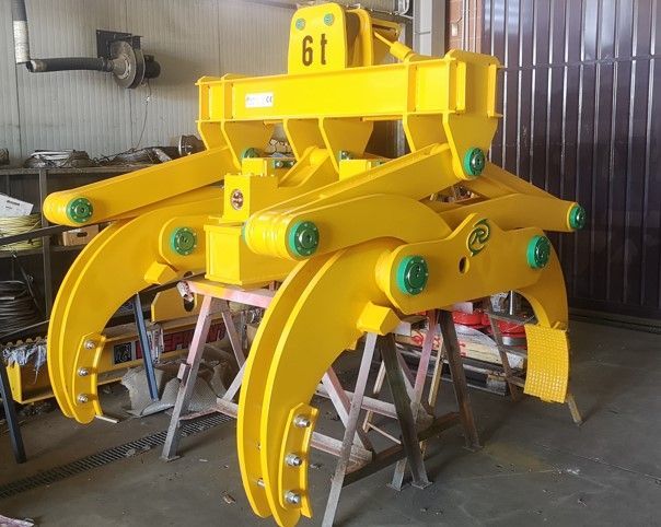 Pinza di sollevamento in metallo giallo con capacità di 6 tonnellate, appoggiata su supporti in legno in un'officina.