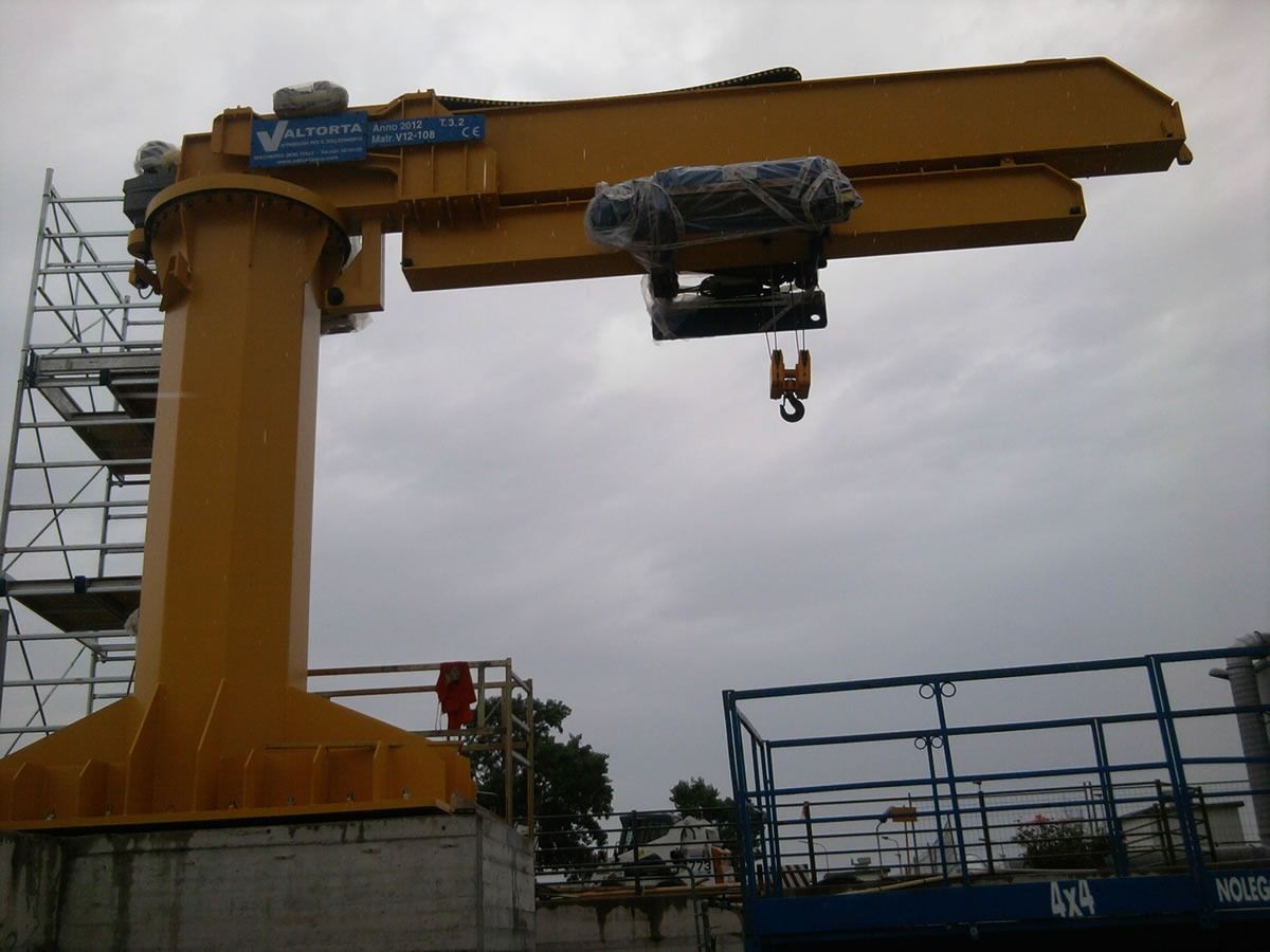 Gru a braccio gialla montata su una base di cemento, estensibile orizzontalmente con un gancio, all'aperto.