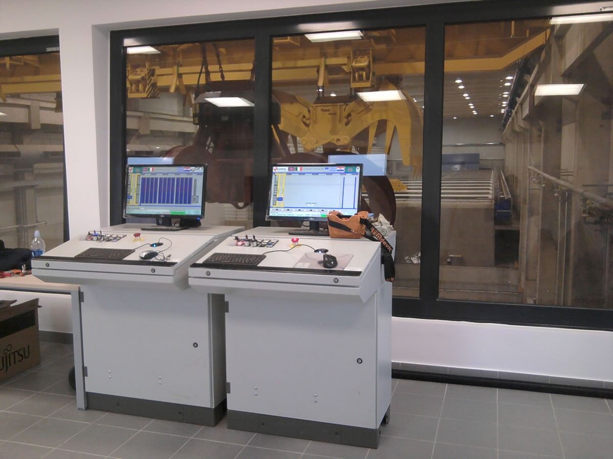 Pannelli di controllo con monitor impostati in fabbrica, visibili attraverso un'ampia finestra.