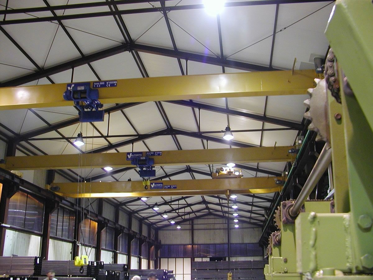 Gru a ponte gialle in un grande edificio industriale con tetto in metallo.