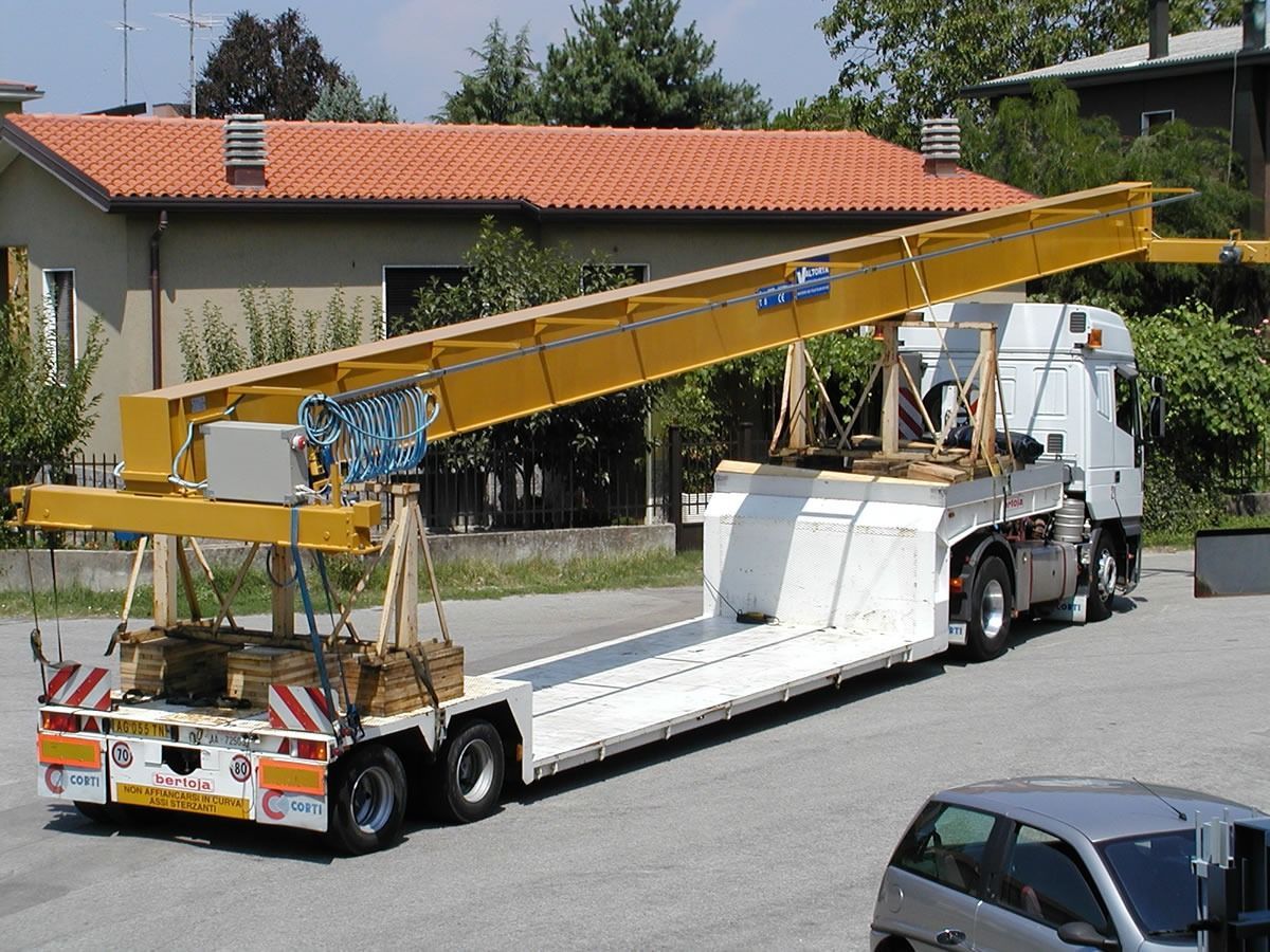 Braccio di una gru gialla montato su un camion con pianale di fronte a un edificio.