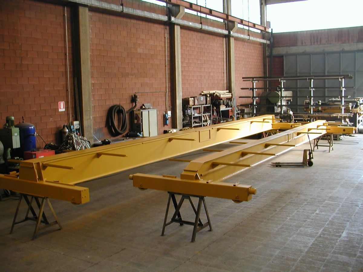 Travi di acciaio giallo su cavalletti in un'officina, probabilmente per lavori edili, contro muri di mattoni.