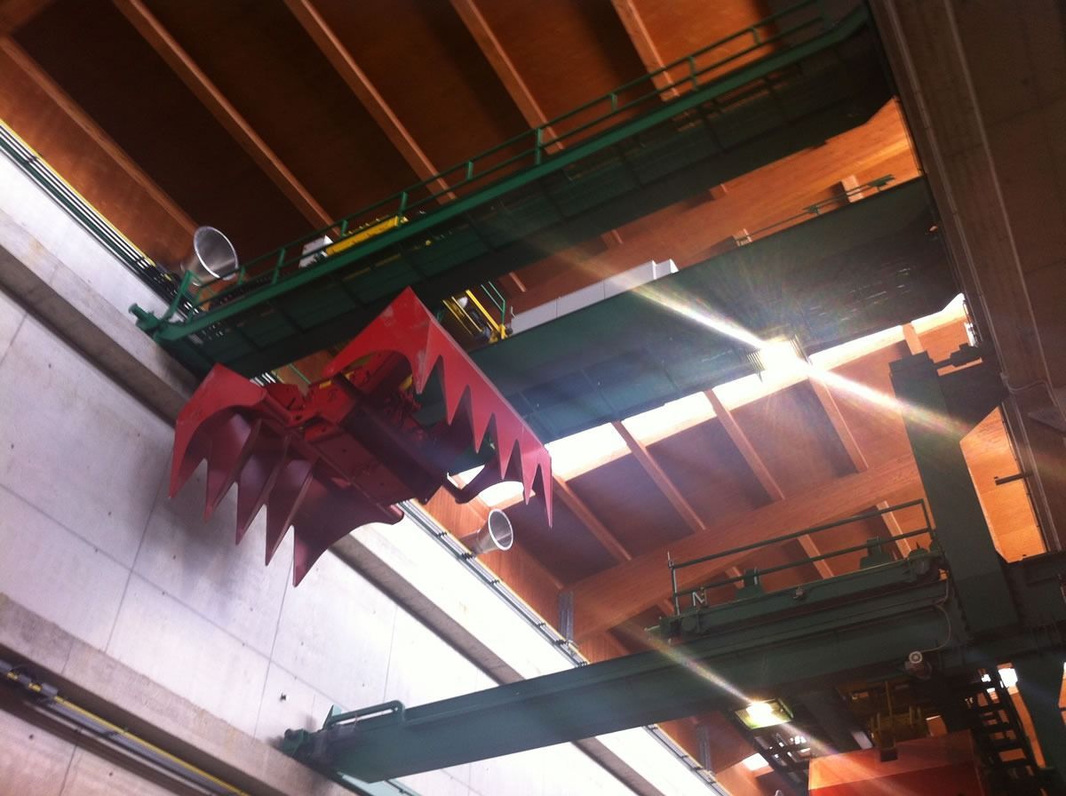 Gru a benna rossa sospesa su travi verdi in un ambiente industriale.