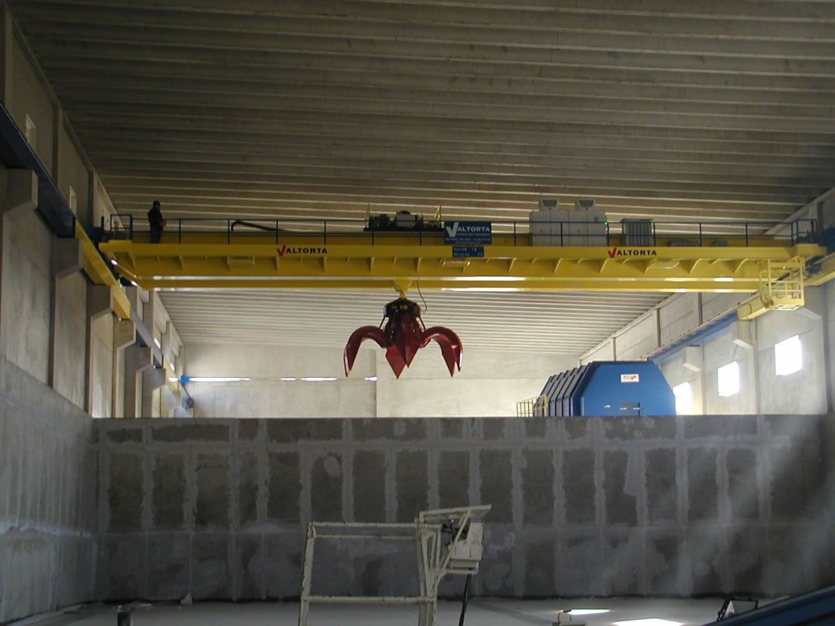 Gru a ponte gialla con pinza in una struttura in cemento.