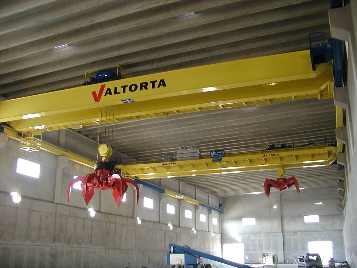 Gru a ponte gialla con rampini rossi all'interno di un magazzino.