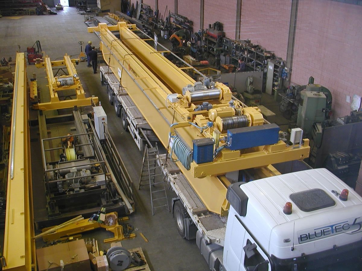 Vista dall'alto: grande gru industriale gialla su un camion a pianale all'interno di un'officina.