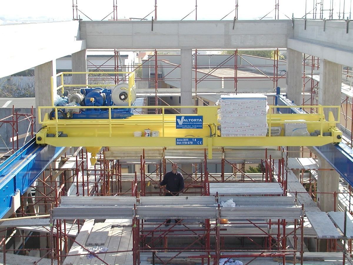 Gru gialla che solleva un grosso blocco in un cantiere edile. Un uomo è in piedi sotto un'impalcatura.