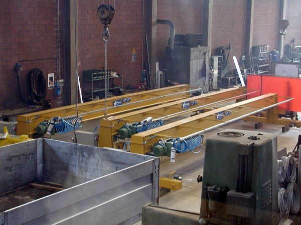 Gru a ponte in una fabbrica, con travi gialle e motori blu, pronte per il sollevamento.