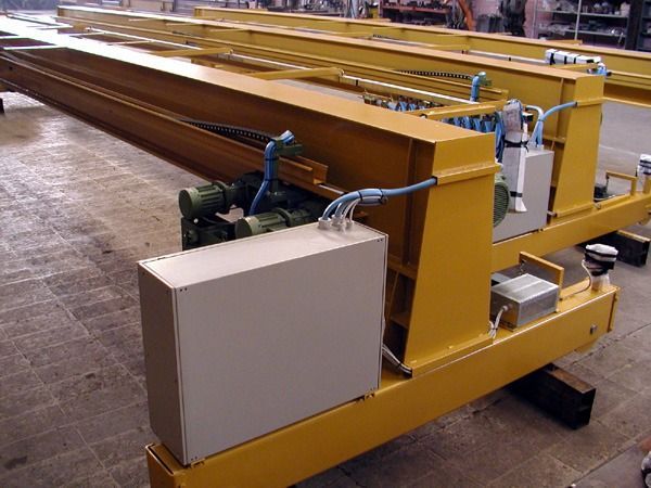 Gru a ponte industriale gialla con quadro elettrico e macchinari in un'officina.