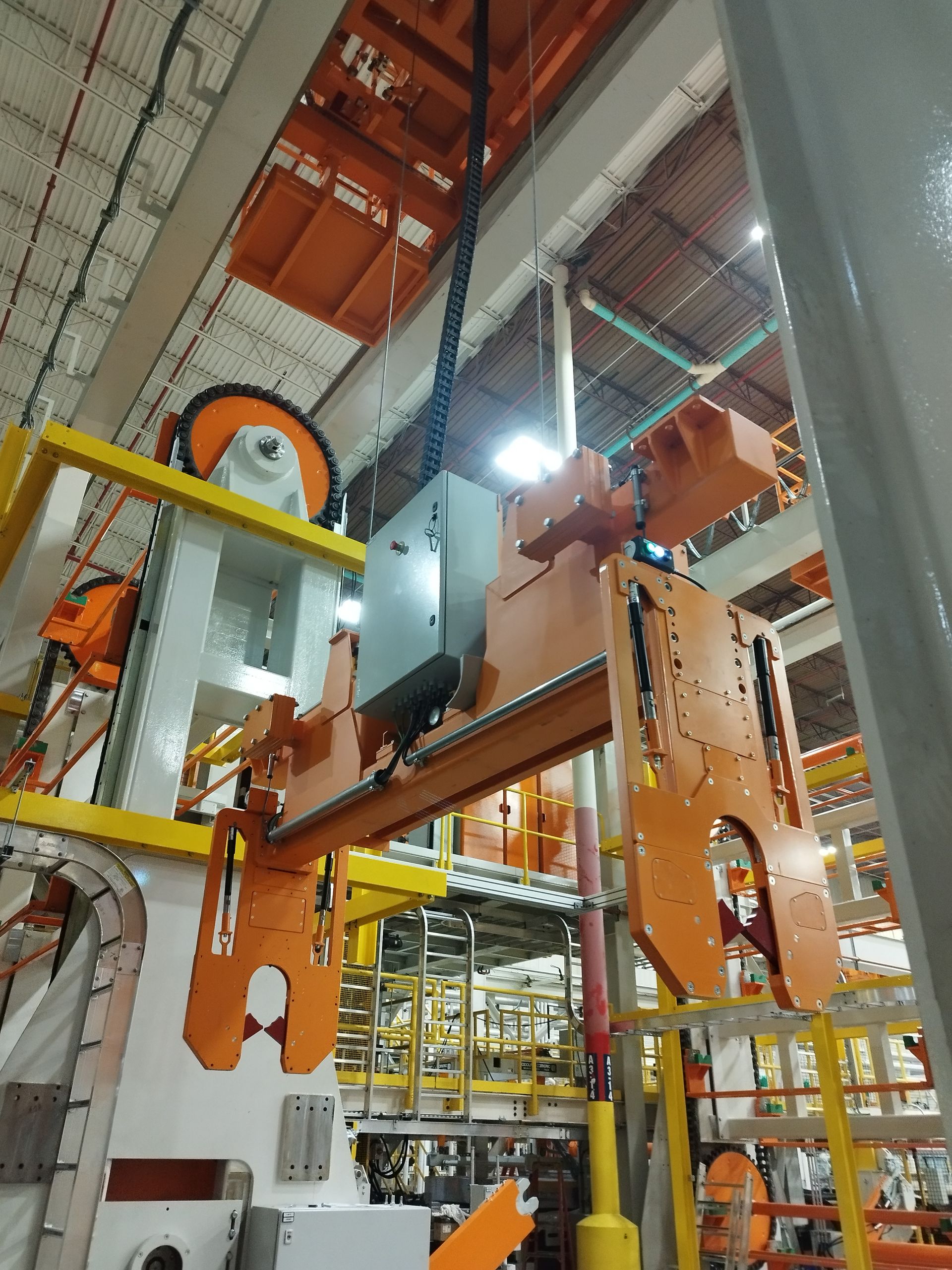 Una gru industriale che solleva attrezzature di colore arancione in un ambiente industriale.