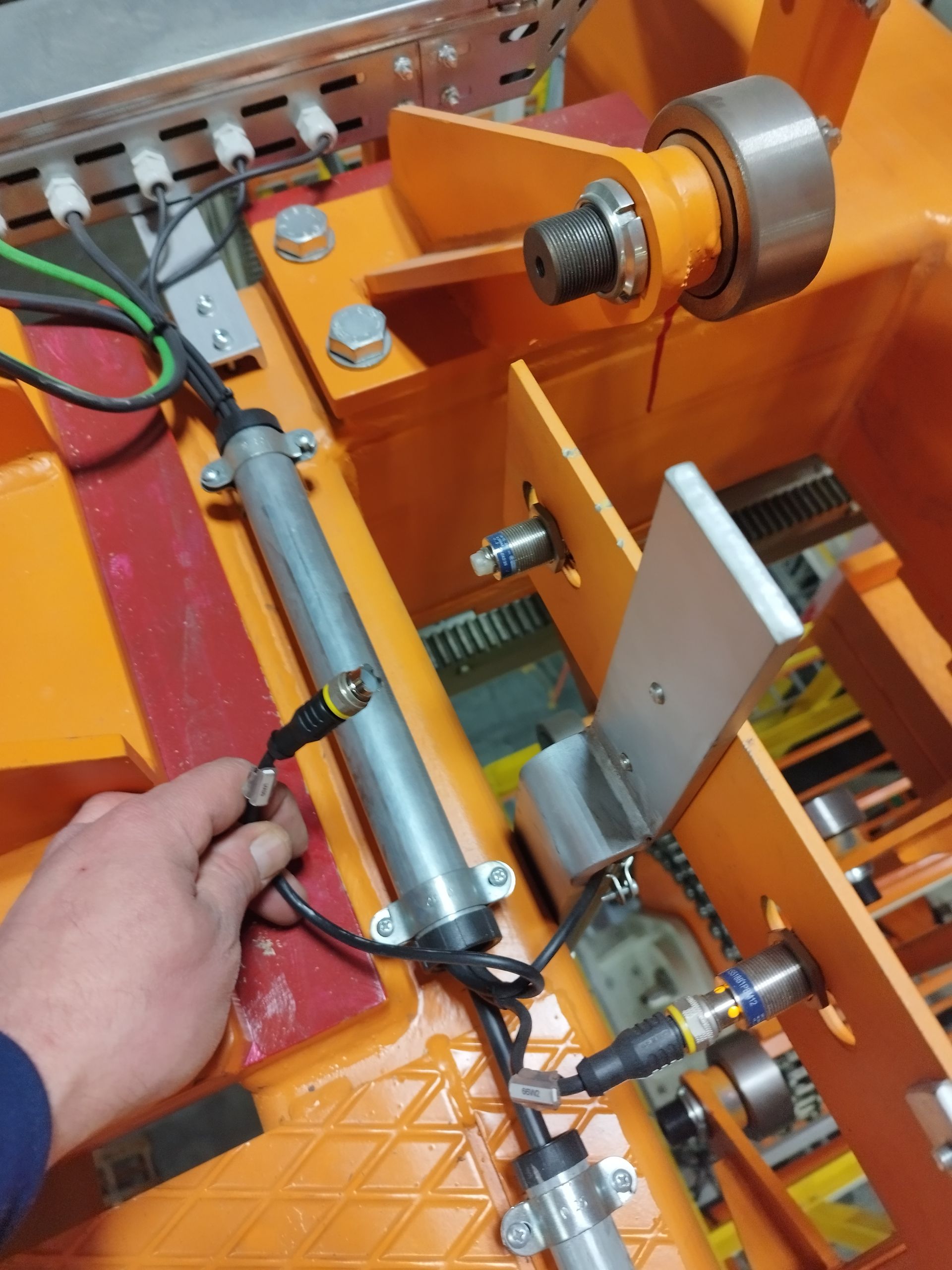 La mano tocca apparecchiature industriali con fili, sensori e una struttura arancione.