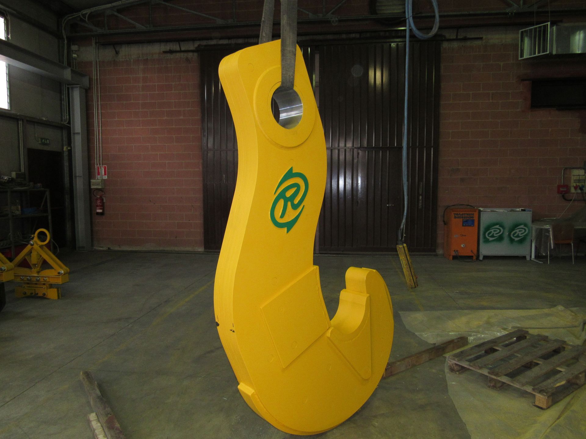 Gancio per gru industriale giallo con logo verde in un magazzino.