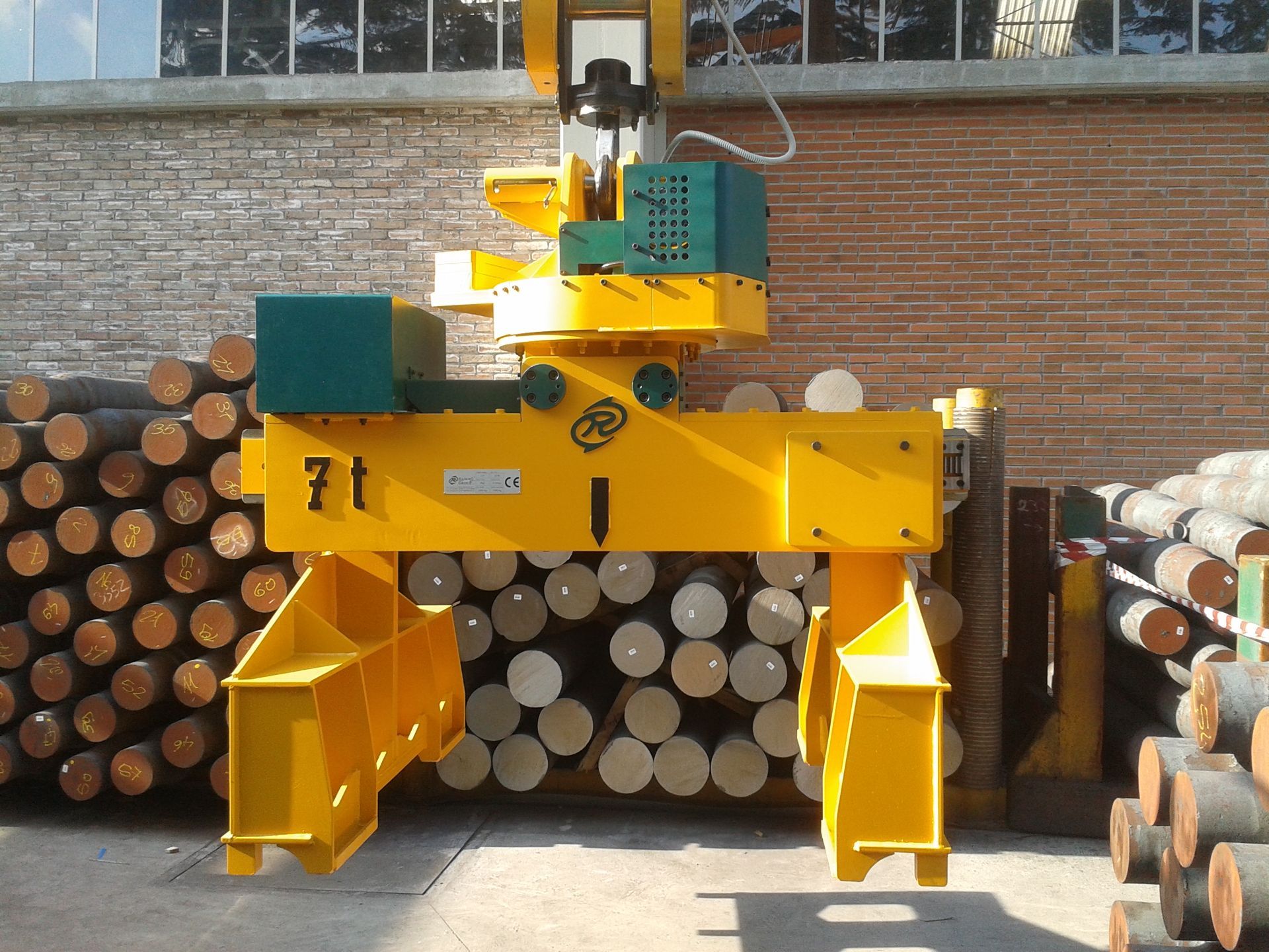 Gru industriale gialla che solleva tronchi cilindrici di metallo in un ambiente industriale.